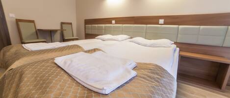 A hotel room with two beds, a wooden headboard, bedside tables, and wall-mounted lights.