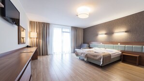 A modern hotel room with a wooden floor, a bed with a headboard, a desk with a flat-screen TV, and a large window with curtains. - Olymp 3 (Kolobrzeg)