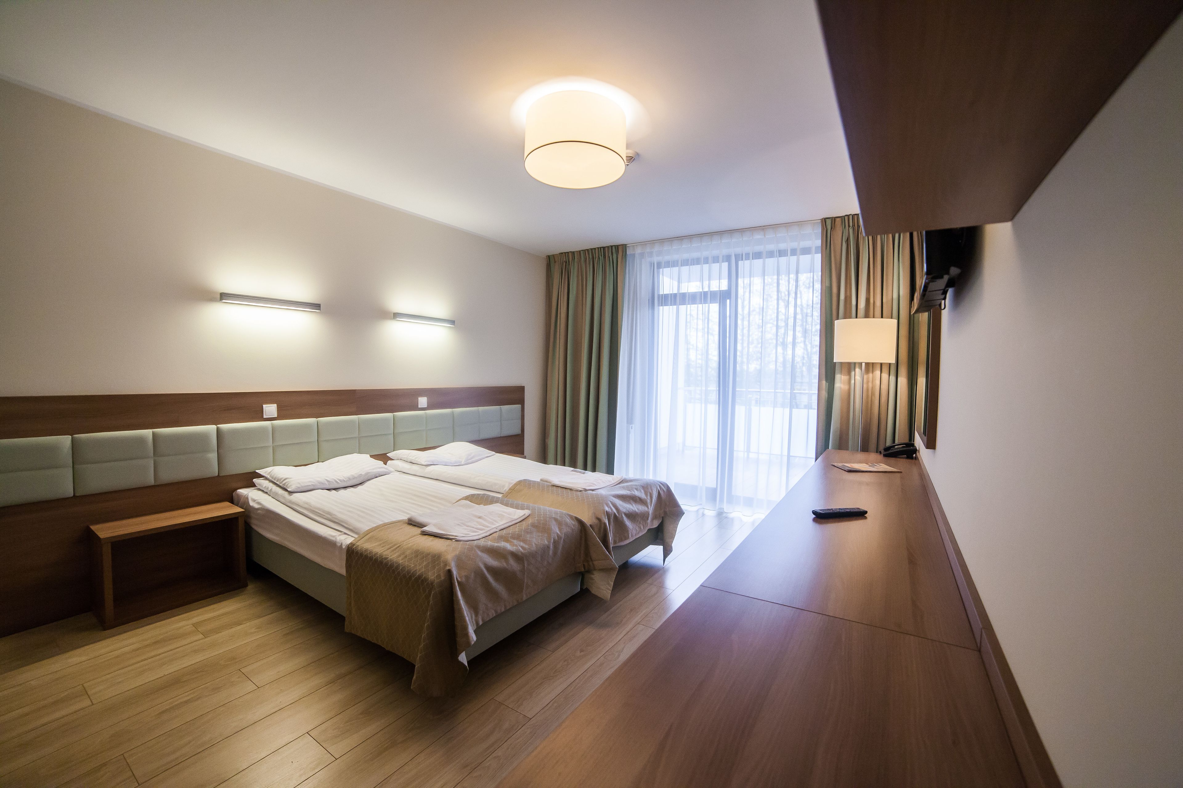 Camera d'albergo con un letto matrimoniale, comodini, abat-jour, una finestra con tende e una lampada a soffitto.