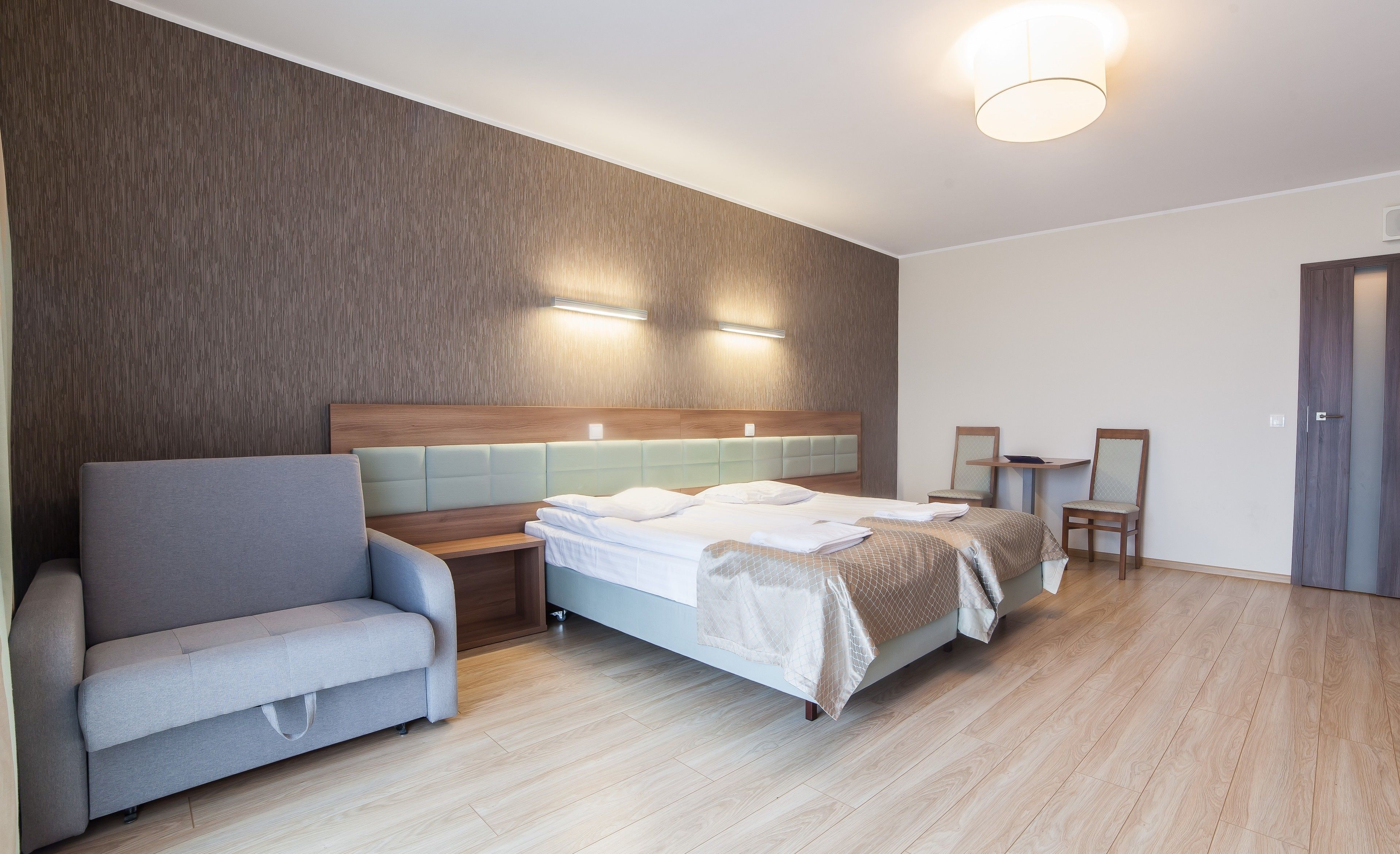 A modern hotel room with a bed, a sofa, a small table, and a chair.