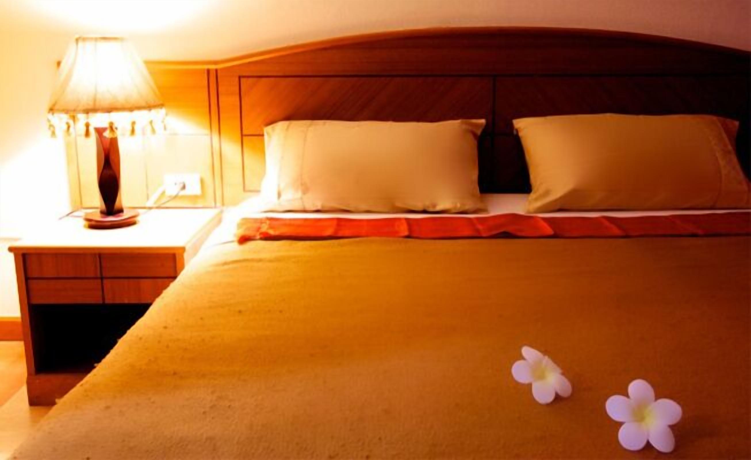 A hotel room with a wooden headboard, a bedside table with a lamp, and two pillows.
