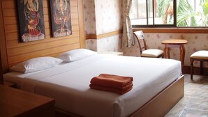 A hotel room with a large bed, wooden headboard, two paintings on the wall, a small round table, and a window with curtains. - Dream Hotel Pattaya (Pattaya)