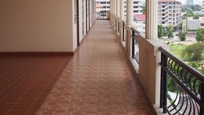 Un couloir au sol carrelé, aux murs blancs, et doté d’un balcon avec une rambarde en métal.