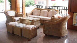 Un ensemble de mobilier de jardin en osier comprenant un canapé, deux fauteuils et une petite table, installé dans un espace extérieur abrité.