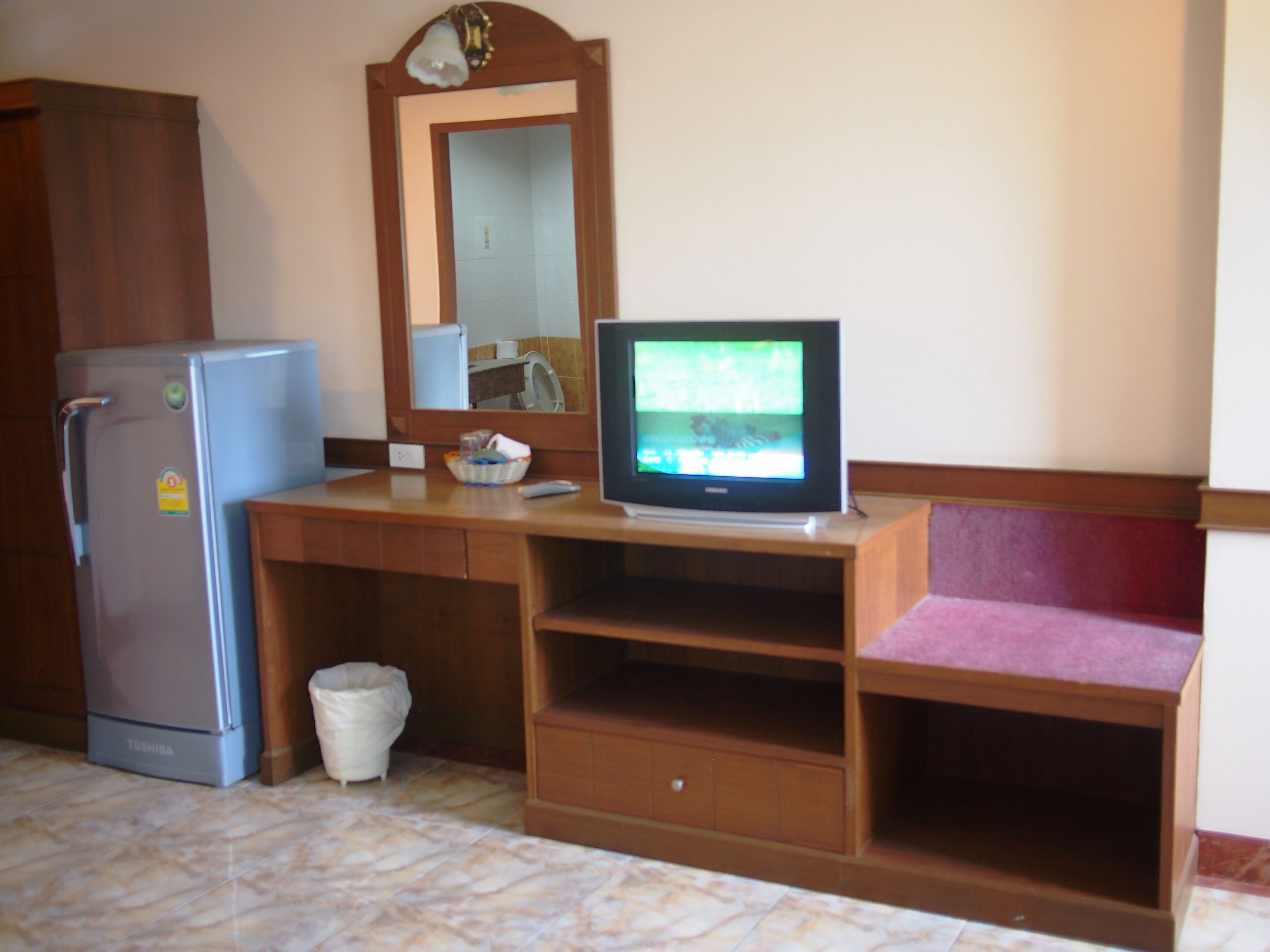 A compact room with a wooden desk, a refrigerator, a television, and a mirror.