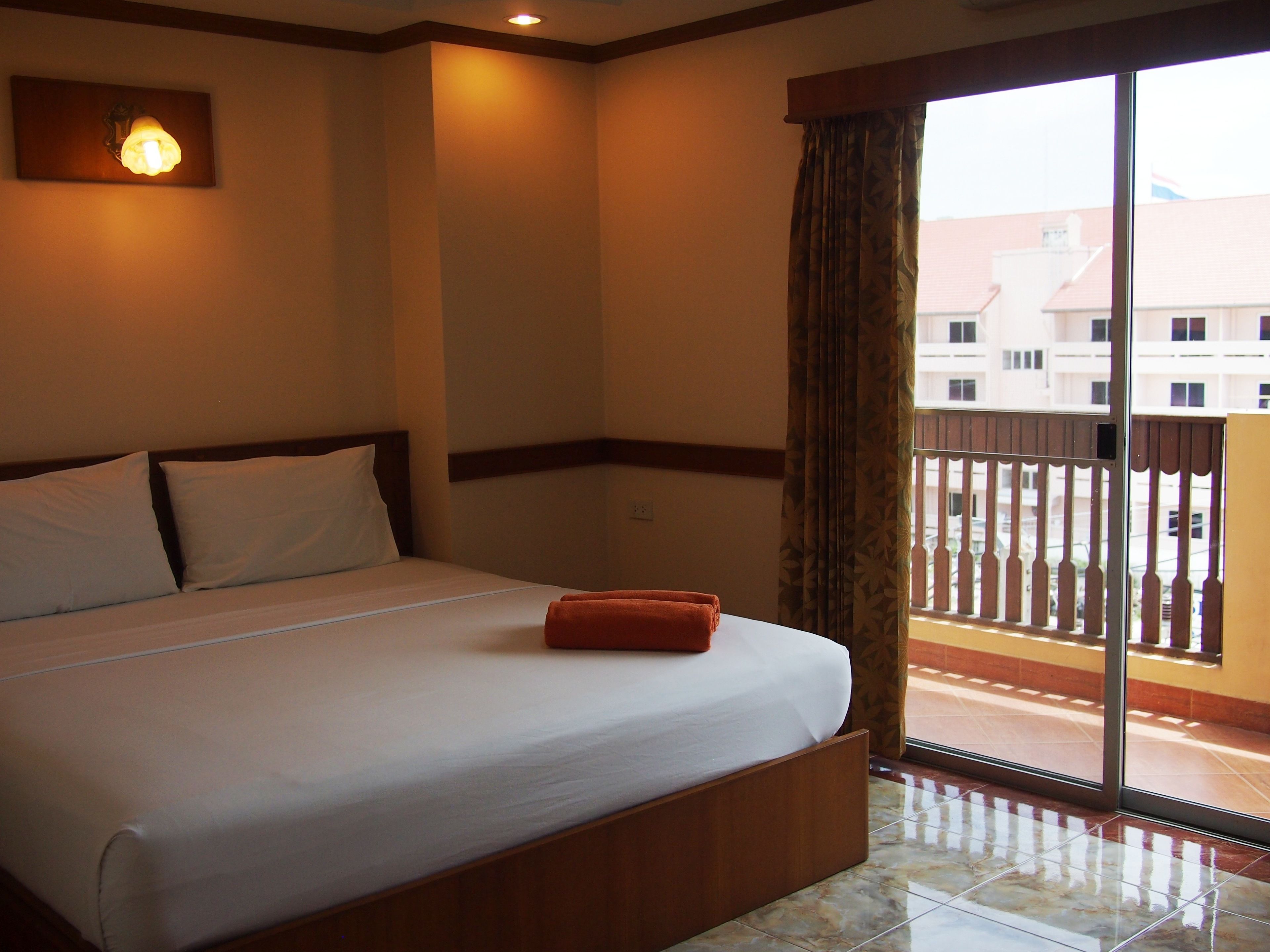 Quarto de hotel com uma cama grande, uma mesa de cabeceira, uma luminária na parede e vista para um edifício pela janela.