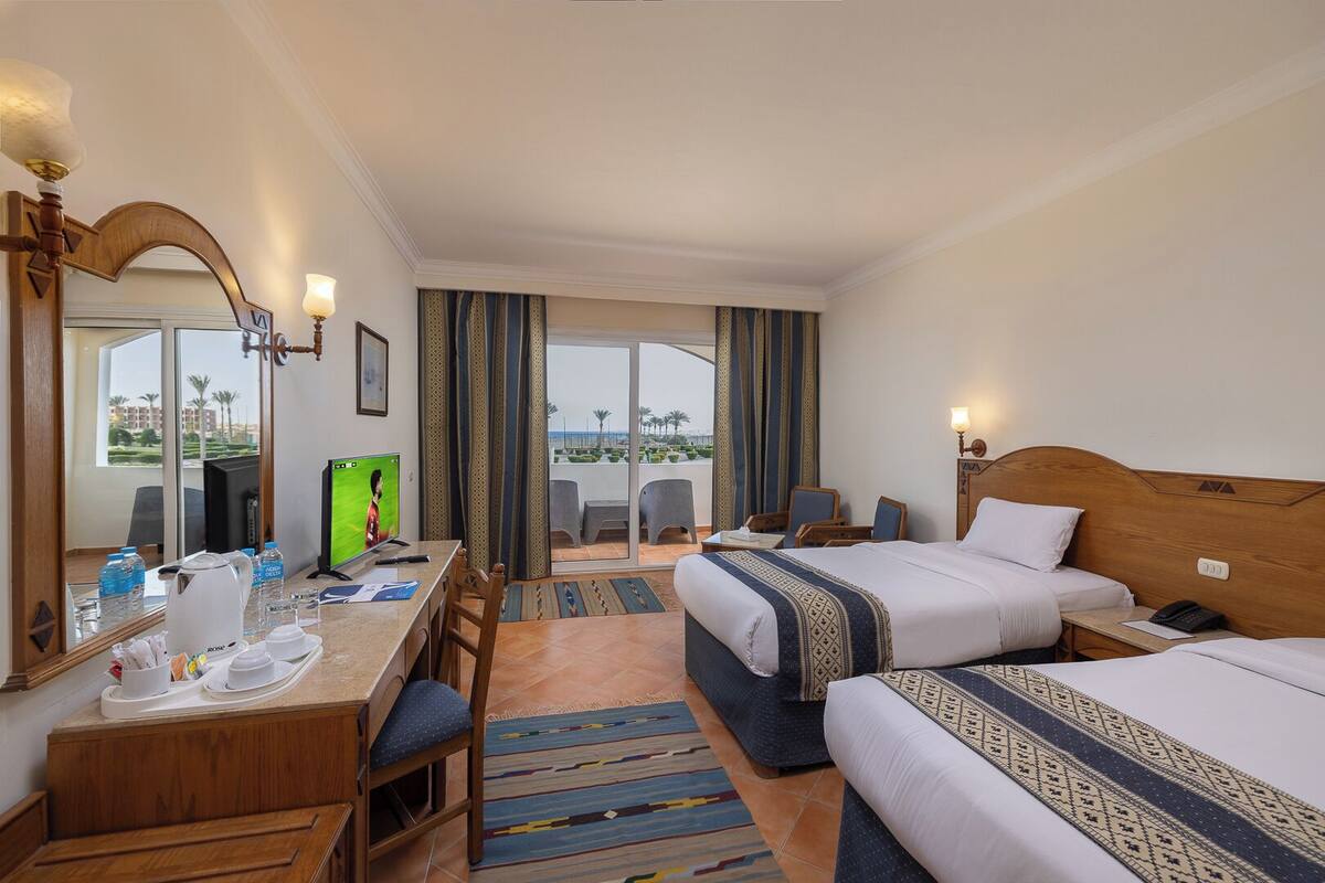 A hotel room with a bed, a desk with a computer, a chair, and a view of the outdoors.
