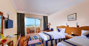 A hotel room with two beds, a television, a desk with a lamp, a chair, and a view of the sea. - Bliss Nada Beach Resort (Marsa Alam)