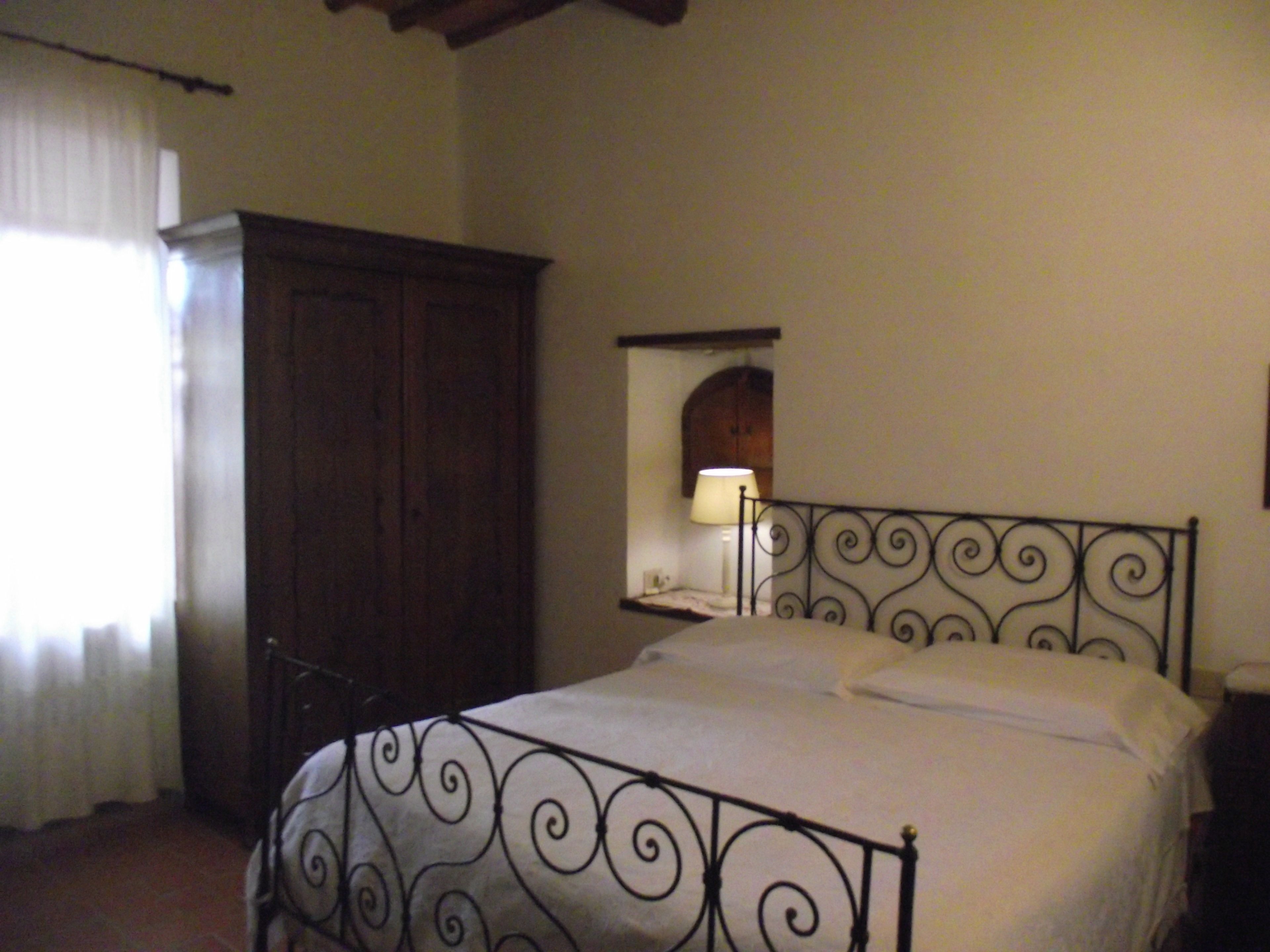 Un dormitorio con una cama, un armario, una mesita de noche, una lámpara y un espejo en la pared.