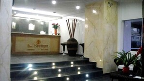 A hotel reception area with a marble reception desk, a staircase with lights, and a potted plant.