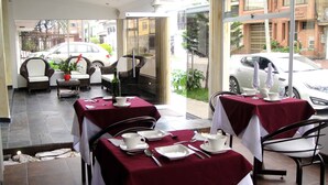 A restaurant with tables set for dining, outdoor seating, and a view of parked cars and buildings.