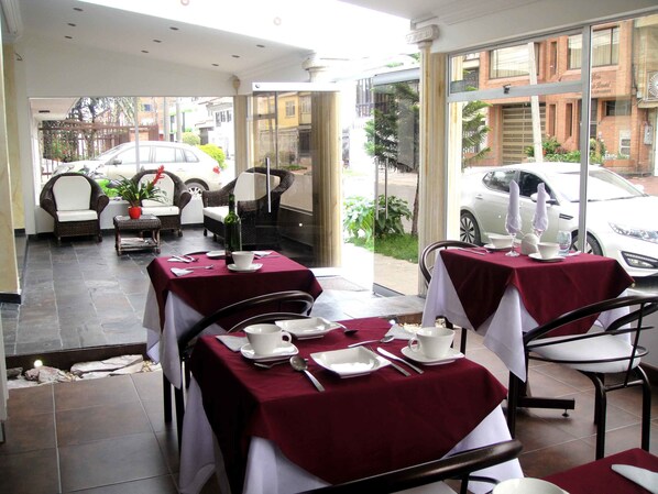 Un restaurant avec des tables dressées pour le service, des places assises en plein air et une vue sur les voitures garées et les bâtiments.