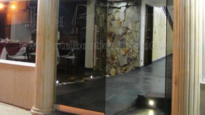 A modern hotel entrance with glass doors, a stone wall, and a seating area visible through the glass.