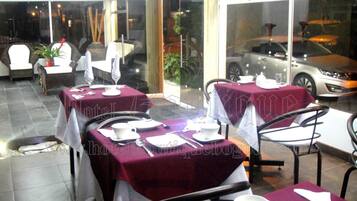 Un restaurante con mesas dispuestas para comer, sillas y un coche visible a través del ventanal.
