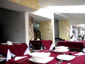 Un espace repas avec des tables dressées, des murs en marbre et une vue sur la rue.