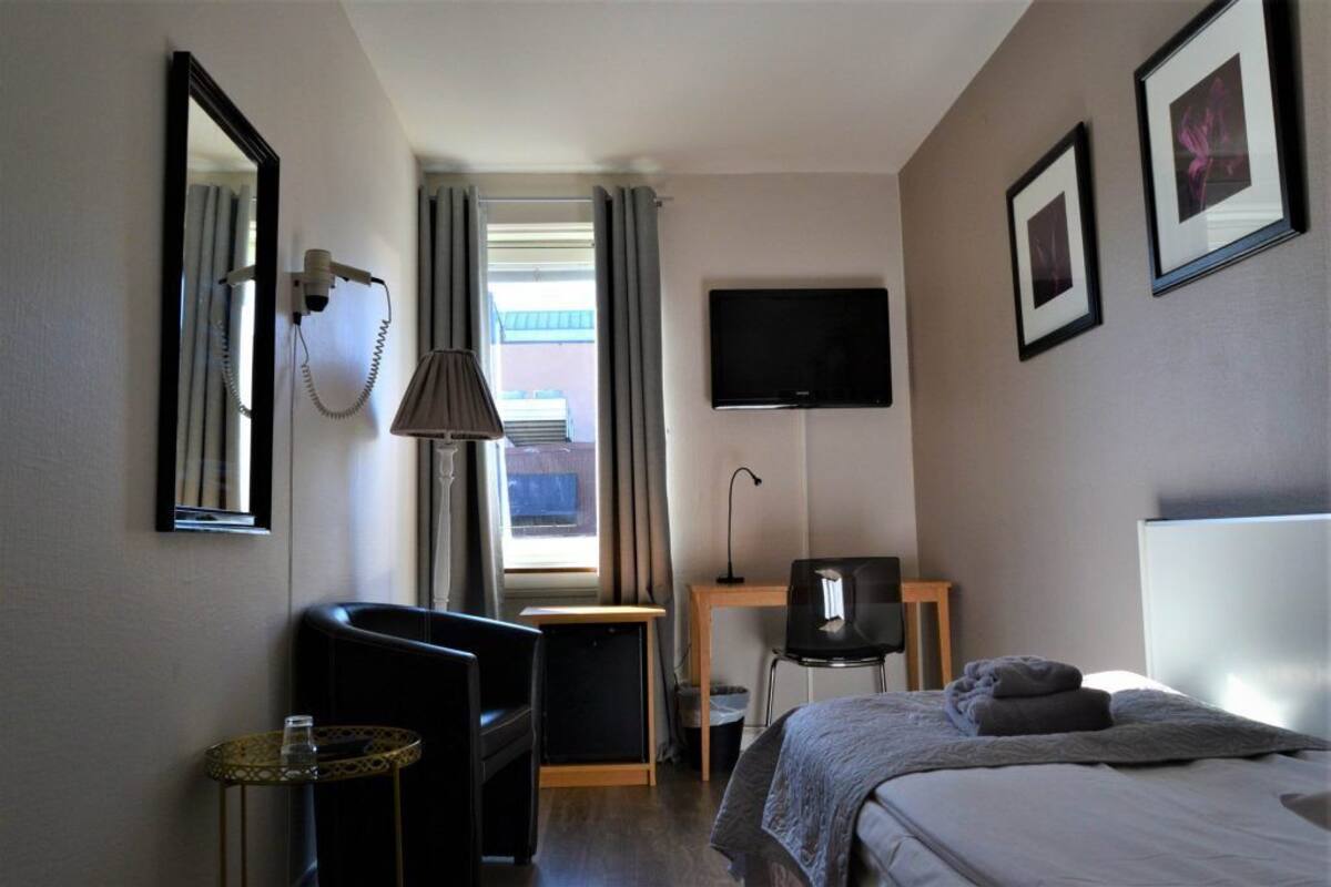 A hotel room with a bed, a desk, a chair, a TV, a mirror, and a window with curtains.