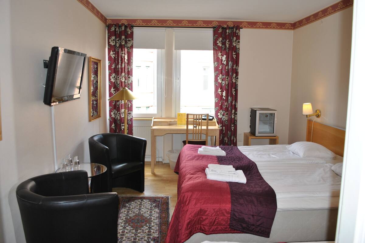 A hotel room with a bed, a desk, a chair, a TV, and a lamp.