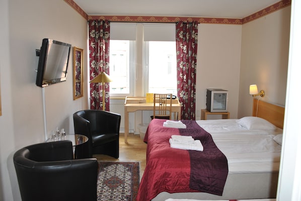 A hotel room with a bed, a desk, a chair, a TV, and a lamp. - Solsta Hotell (Karlstad)