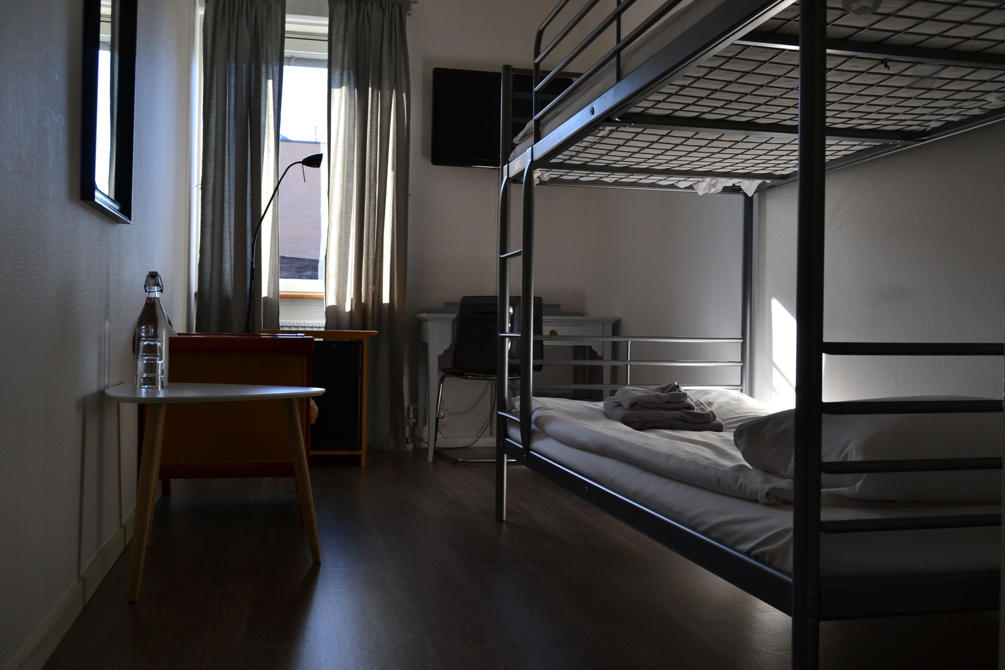 Une chambre avec un lit superposé, un bureau, une chaise et une bouteille posée sur le bureau.