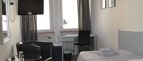 Una habitación de hotel con cama, escritorio, silla, televisor y ventana con cortinas.