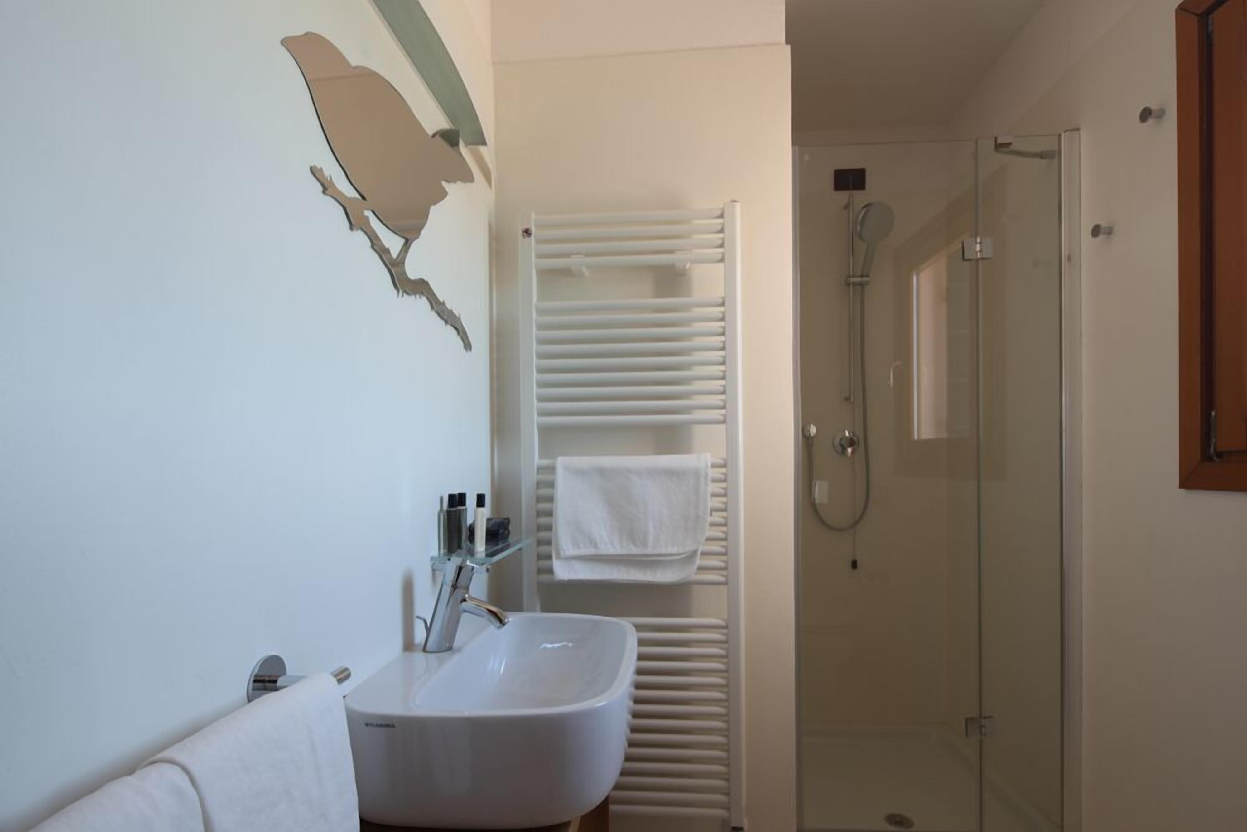 A bathroom with a white sink, a glass shower enclosure, and a towel rack with multiple towels.