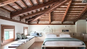 Une chambre avec un plafond en pente, des banquettes intégrées, un lit avec des oreillers, des lampes de chevet et une fenêtre avec des stores.
