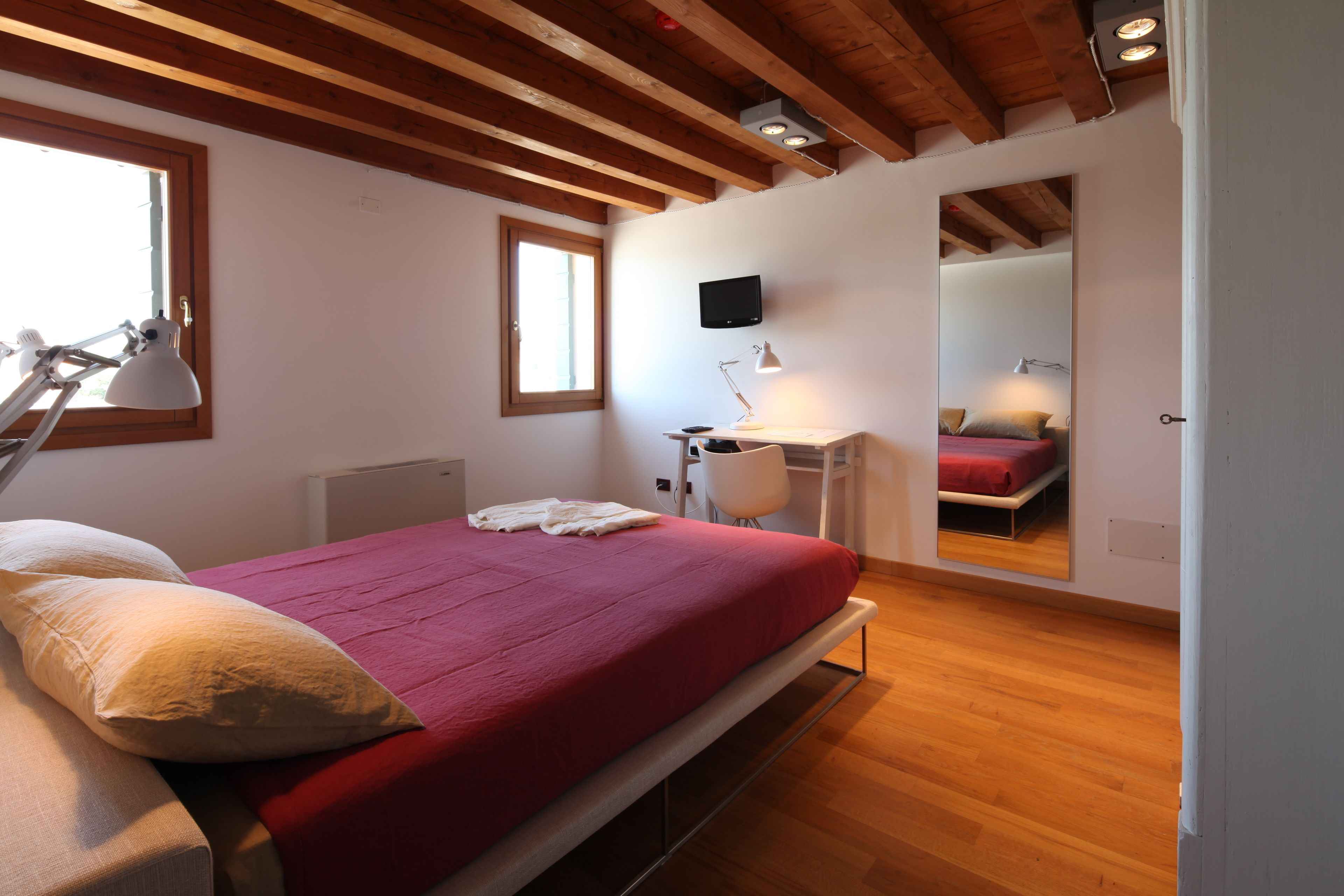 A bedroom with a bed, bedside lamps, a desk, and a mirror.