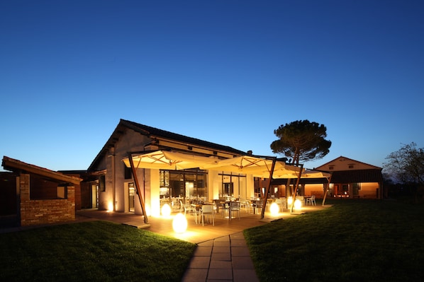 Une maison moderne dotée d’un patio couvert, d’un espace salon extérieur et d’une entrée bien éclairée.