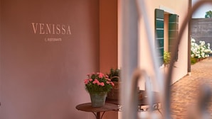 Un bâtiment sur lequel on peut lire les noms « VENISSA » et « IL RISTORANTE ». Au premier plan, on aperçoit une petite table sur laquelle est posée une plante en pot.