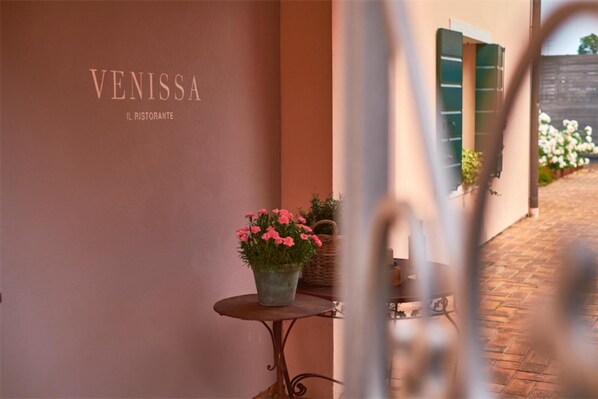 A building with the name 'VENISSA' and 'IL RISTORANTE' on the wall. There is a small table with a potted plant in the foreground. - Venissa Wine Resort (Mazzorbo)