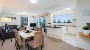 A modern living room with a sofa, TV, and dining area. - The Ritz Resort (Broadbeach)