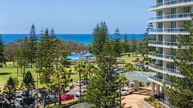 A high-rise hotel with multiple balconies overlooking a coastal area, a parking lot, and a small blue tent structure. - The Ritz Resort (Broadbeach)