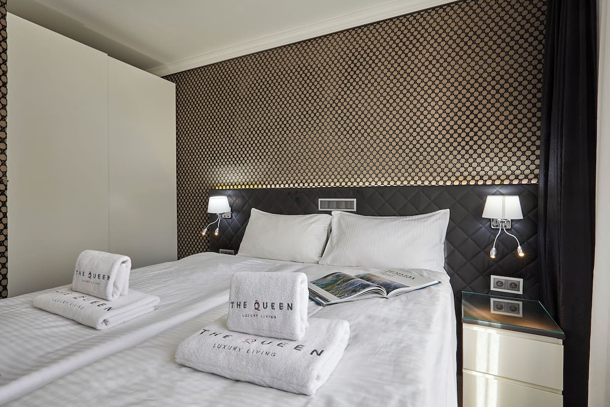 Ein Hotelzimmer mit einem großen Bett, zwei Kissen, einer Zeitschrift und zwei gefalteten Handtüchern mit dem Aufdruck "The Queen Luxury Living".