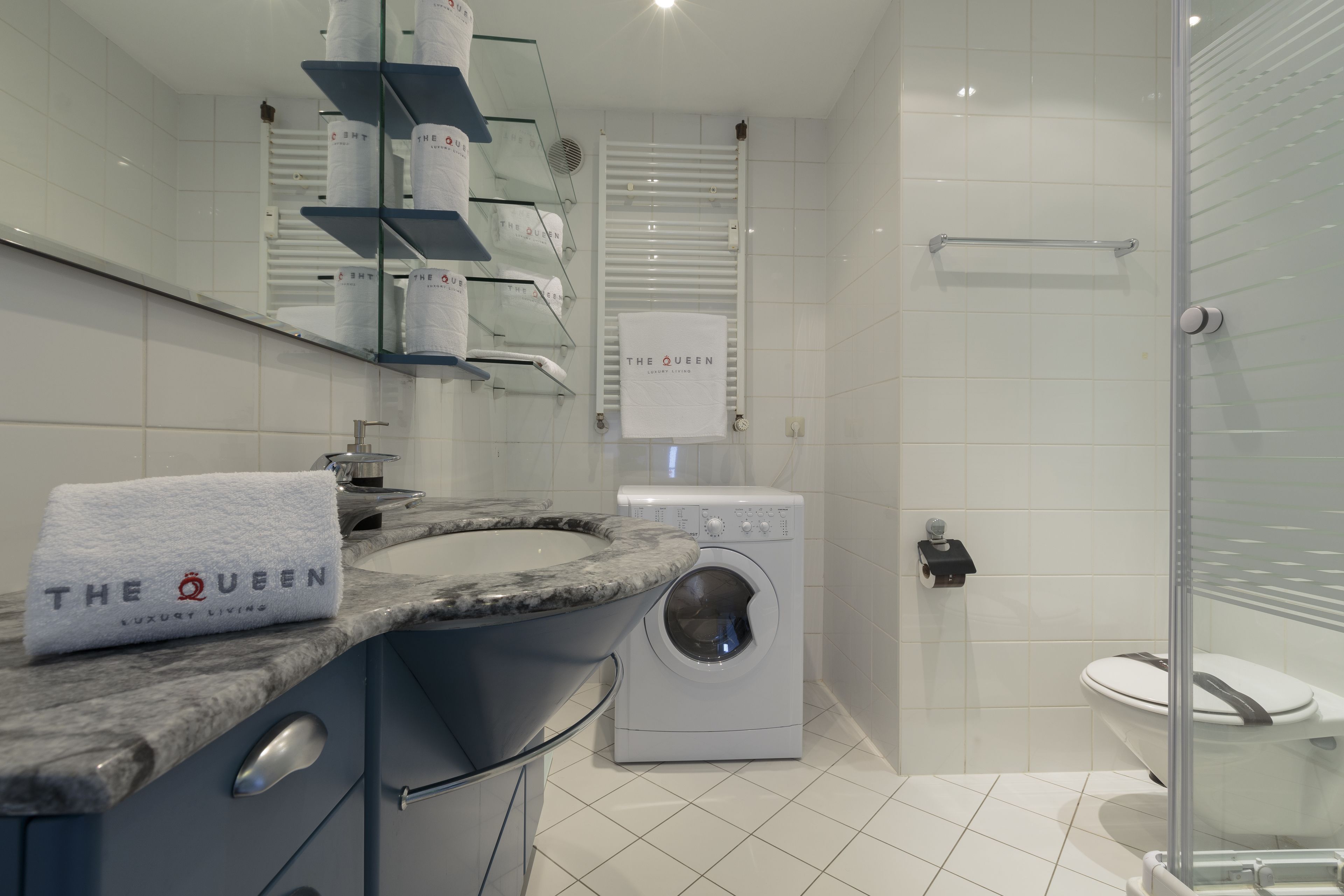 A modern bathroom with a marble sink, a washing machine, a toilet, and a glass shower enclosure.