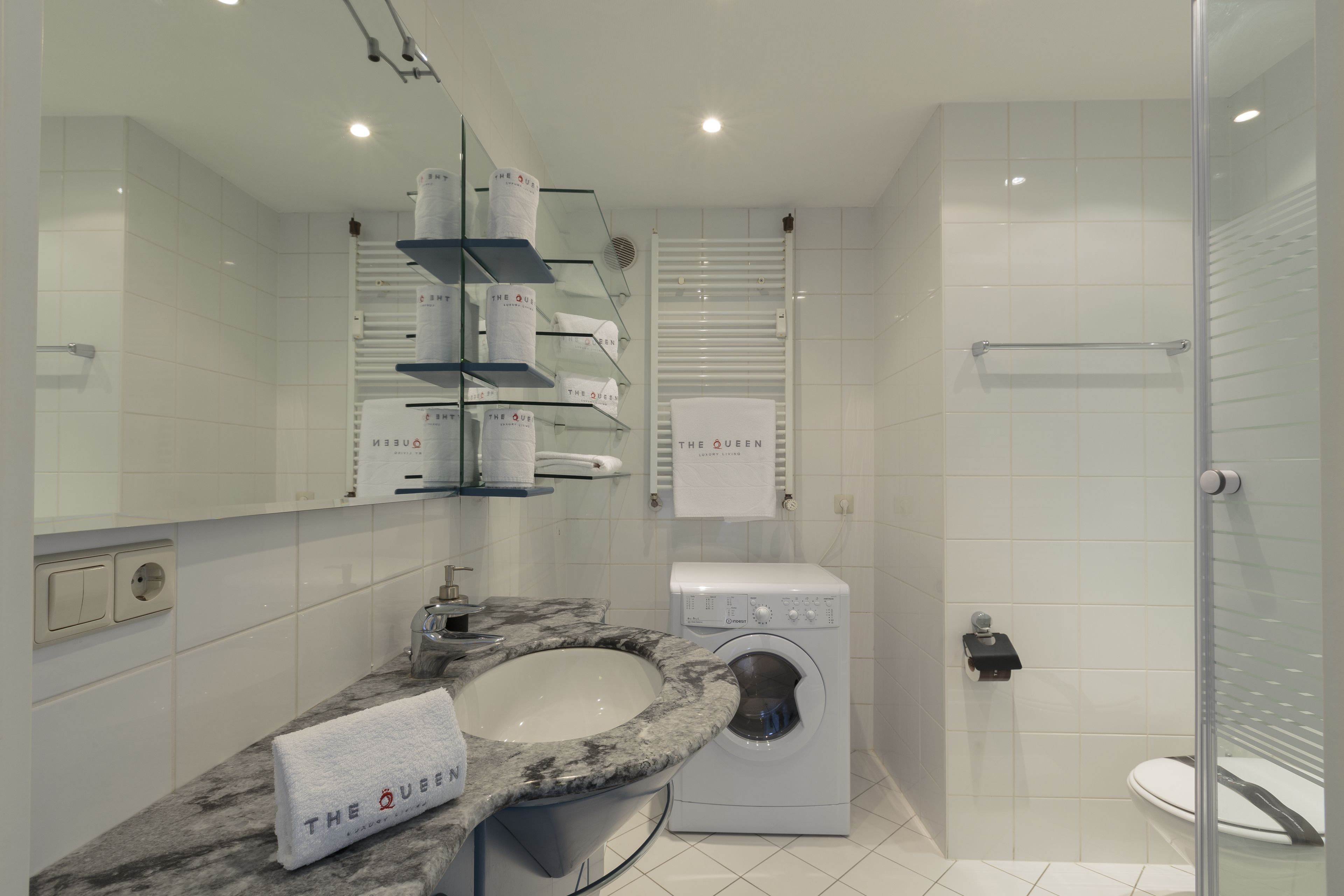 A modern bathroom with a marble sink, a washing machine, and a glass shower enclosure.
