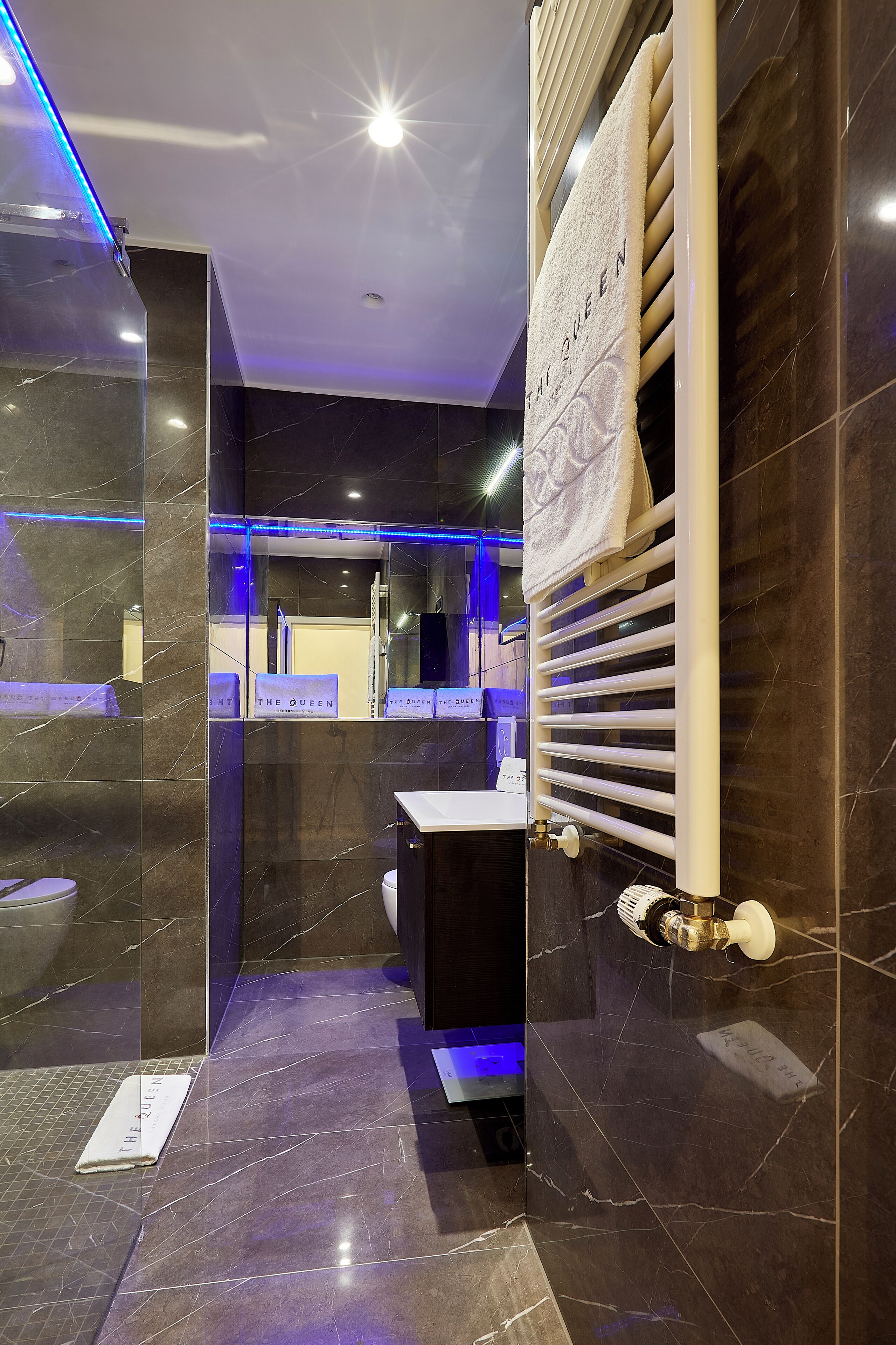 A modern bathroom with dark marble tiles, a white towel rack, and a visible sink.