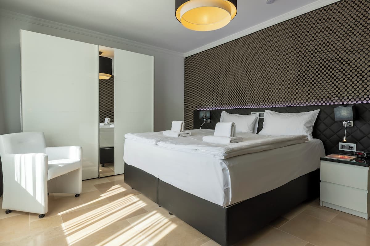 Ein modernes Hotelzimmer mit einem großen Bett, einem weißen Stuhl, einem Nachttisch und einer Wand mit Muster.