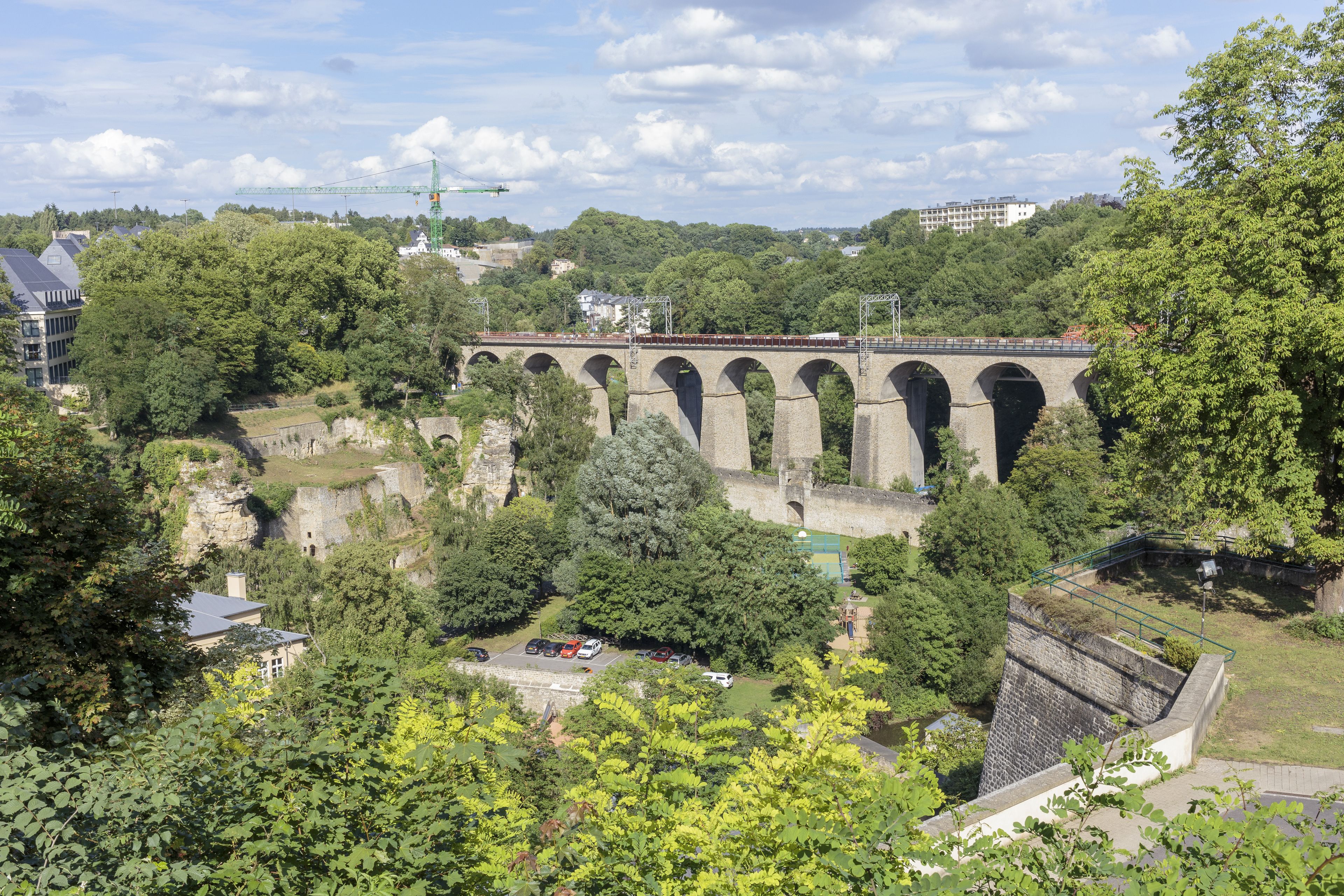 A stone viaduct with multiple arches, surrounded by lush greenery and trees.