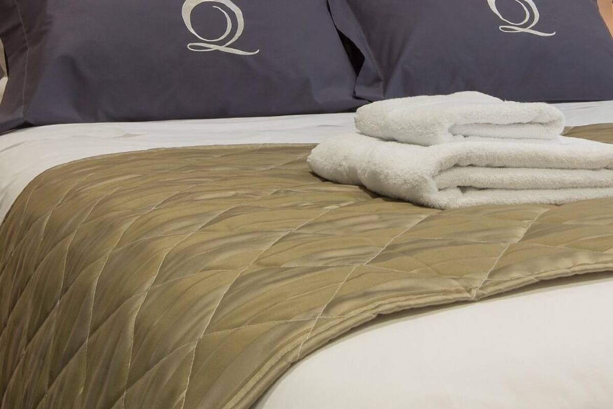 Cama com colcha bege e dois travesseiros com desenho branco bordado.