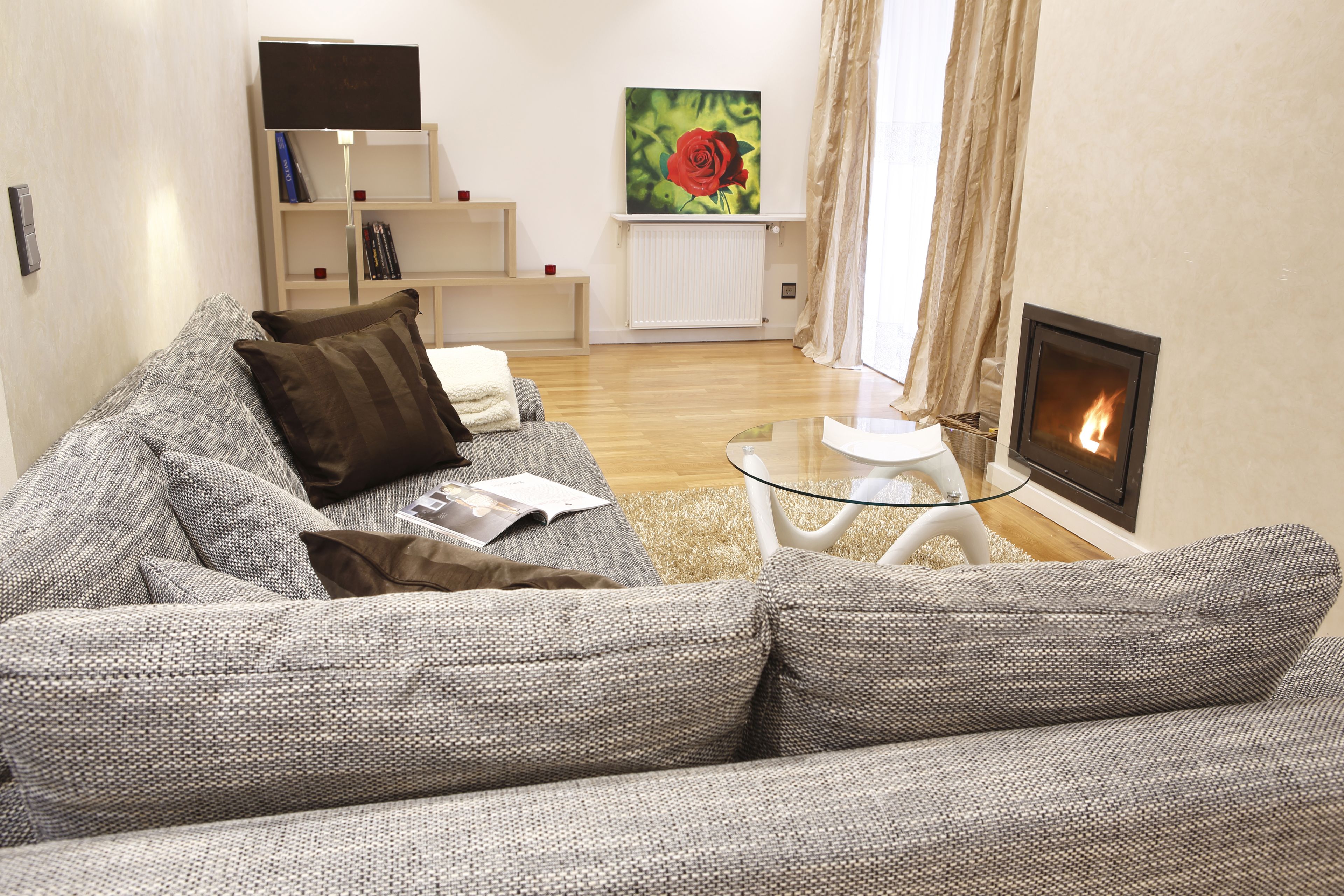 Ein Wohnzimmer mit grauem Sofa, einem Glastisch, einem Kamin und einem Bücherregal mit Büchern und einem Fernseher.