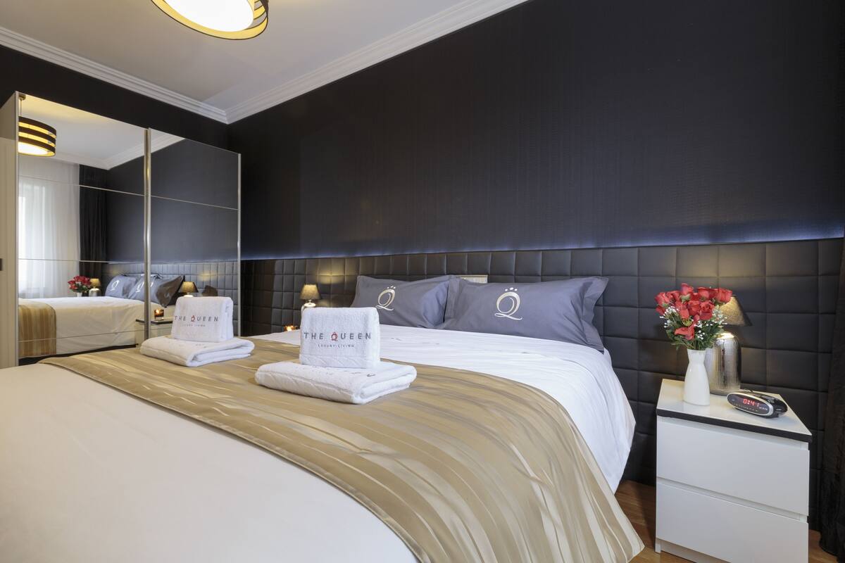 Quarto de hotel moderno com uma cama grande, uma mesa de cabeceira, um espelho e cabeceira escura.