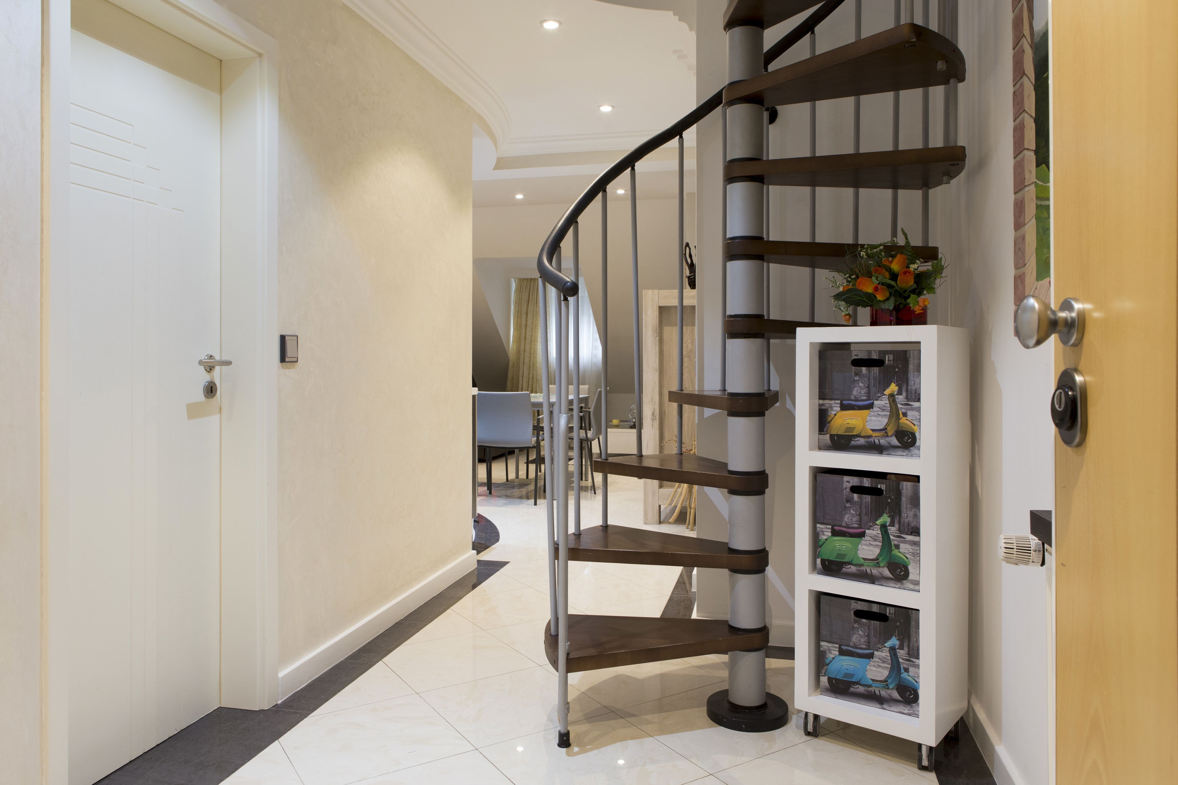Een modern interieur met een wenteltrap, een witte kast met speelgoed en een eethoek op de achtergrond.