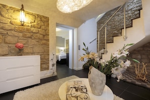 A modern interior with a stone wall, a white console, and a staircase with metal railings.
