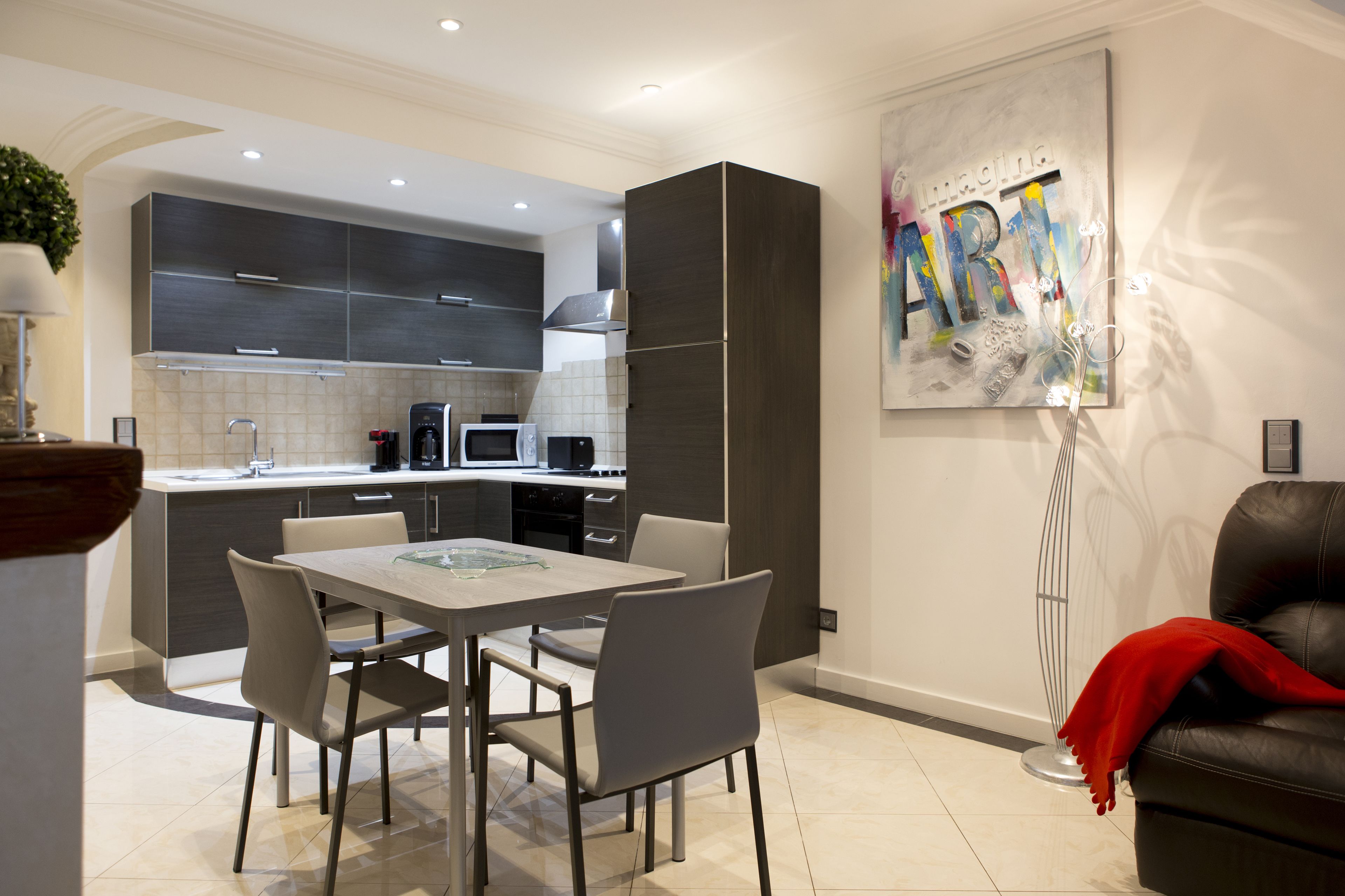A modern kitchen with dark cabinetry, a dining table with chairs, and a red throw on a leather sofa.