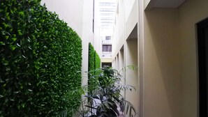 A narrow indoor corridor with a green hedge on one side and a white wall on the other. - Sofyan Hotel Soepomo (Jakarta)