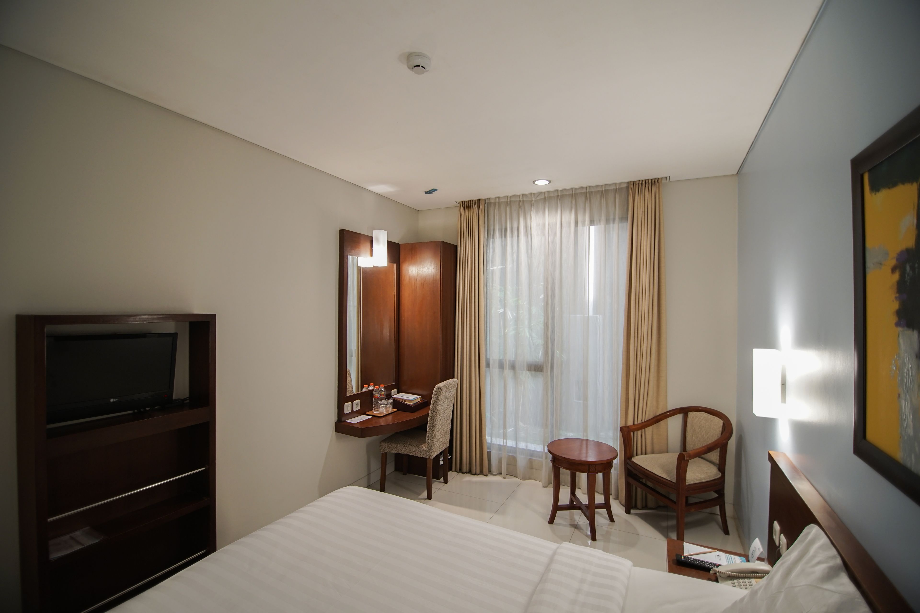 A hotel room with a bed, a desk with a chair, a television, and a large window with curtains.