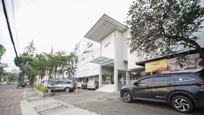 A modern hotel with a prominent sign, a covered entrance, and a parking area with several cars. - Sofyan Hotel Soepomo (Jakarta)