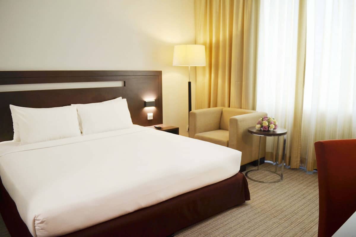 A hotel room with a large bed, a bedside table, a lamp, a chair, and a small table with flowers.