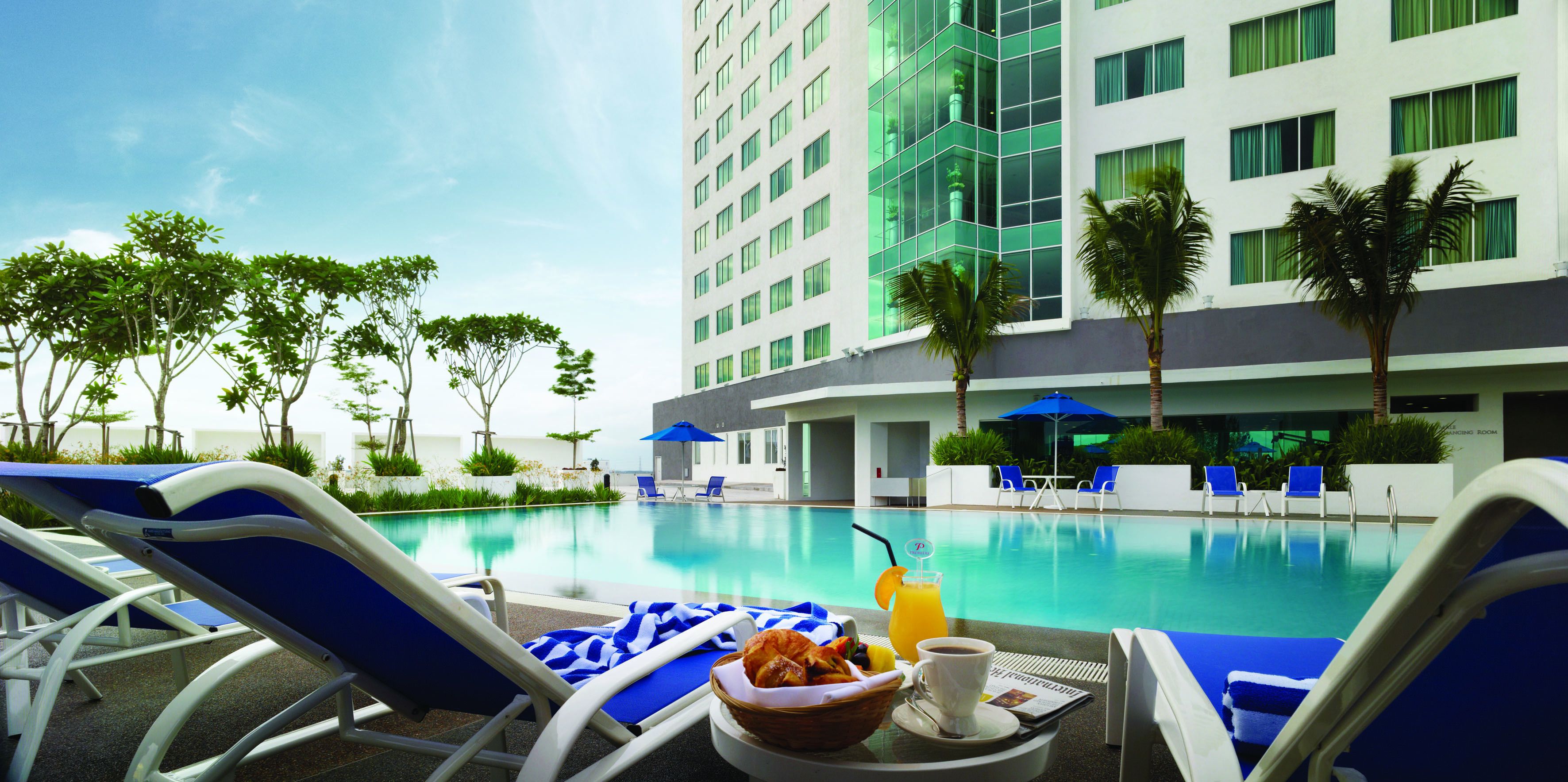 A hotel pool area with lounge chairs, a dining table with breakfast, and a modern building in the background.
