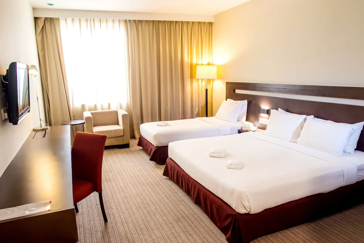 A hotel room with two beds, a desk, a chair, a TV, and a window with curtains.